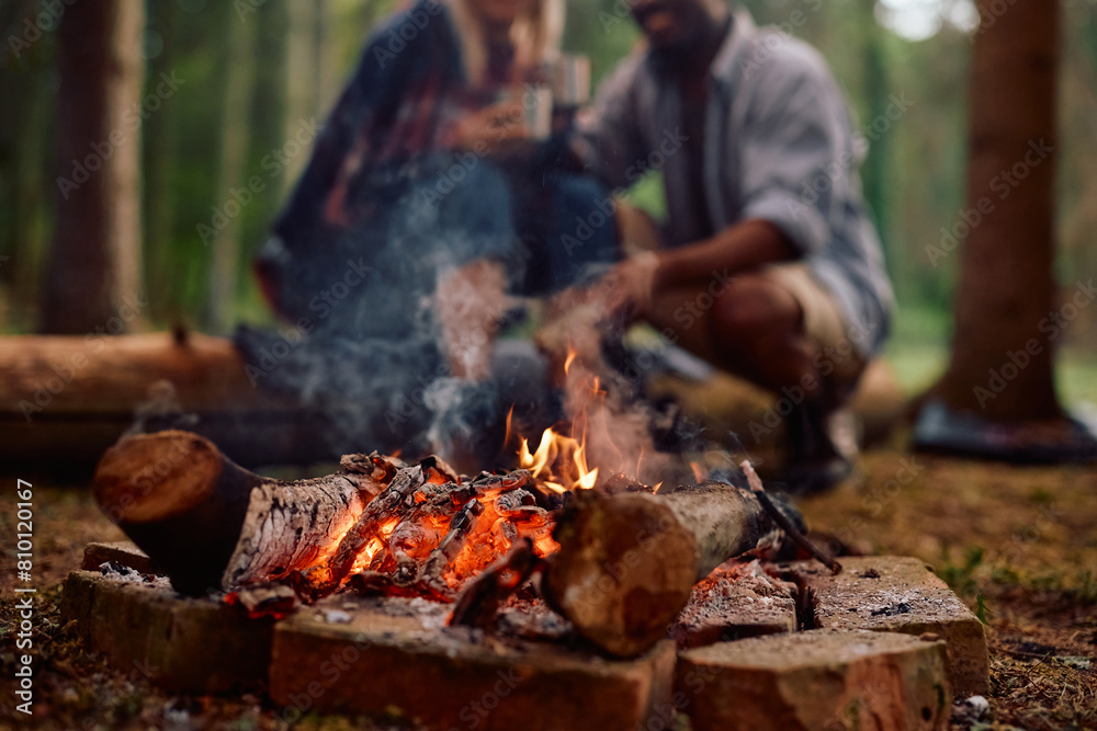 Fototapeta premium Close up of campfire with couple in background.