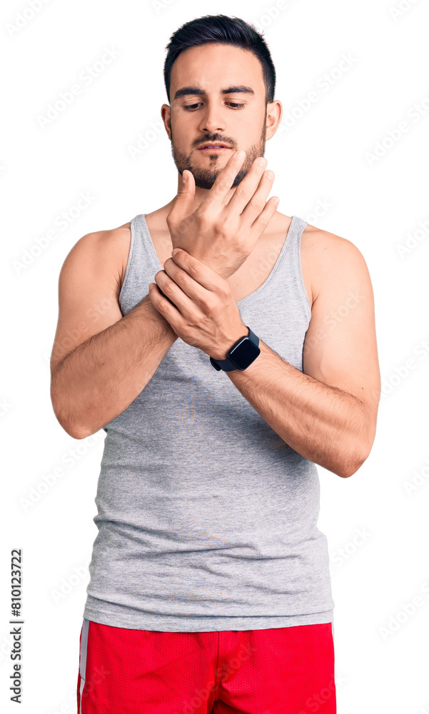 Young handsome man wearing swimwear and sleeveless t-shirt suffering pain on hands and fingers, arthritis inflammation Young handsome man wearing swimwear and sleeveless t-shirt suffering pain on hands and fingers, arthritis inflammation