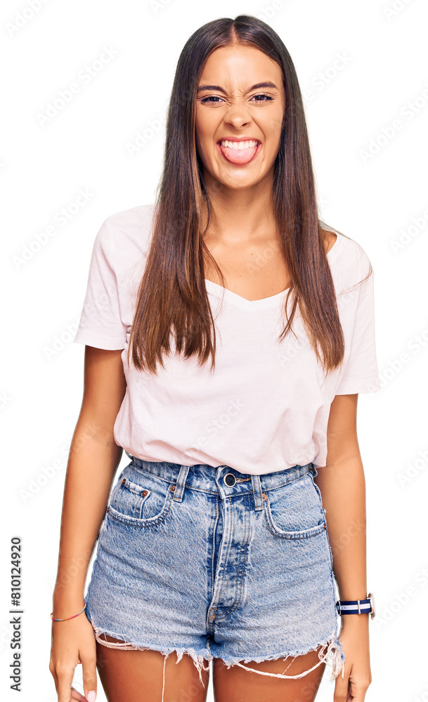 Young hispanic woman wearing casual white tshirt sticking tongue out happy with funny expression. emotion concept. Young hispanic woman wearing casual white tshirt sticking tongue out happy with funny expression. emotion concept.