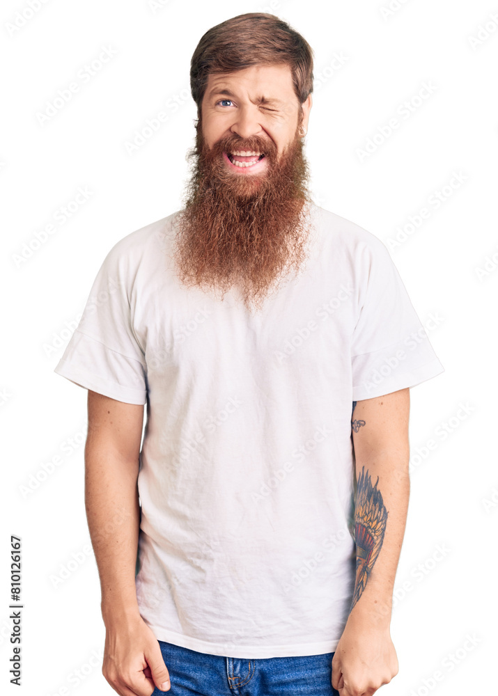 Handsome young red head man with long beard wearing casual white tshirt winking looking at the camera with sexy expression, cheerful and happy face. Handsome young red head man with long beard wearing casual white tshirt winking looking at the camera with sexy expression, cheerful and happy face.