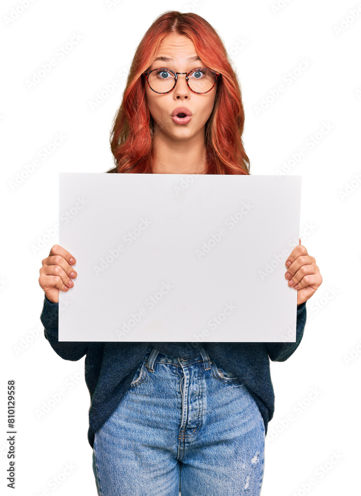 Young redhead woman holding blank empty banner scared and amazed with open mouth for surprise, disbelief face Young redhead woman holding blank empty banner scared and amazed with open mouth for surprise, disbelief face