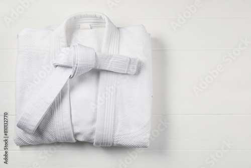 White karate belt and kimono on wooden background, top view. Space for text