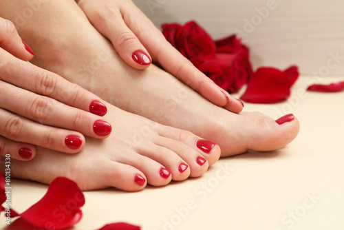 Woman with stylish red toenails after pedicure procedure and rose petals on beige background  closeup