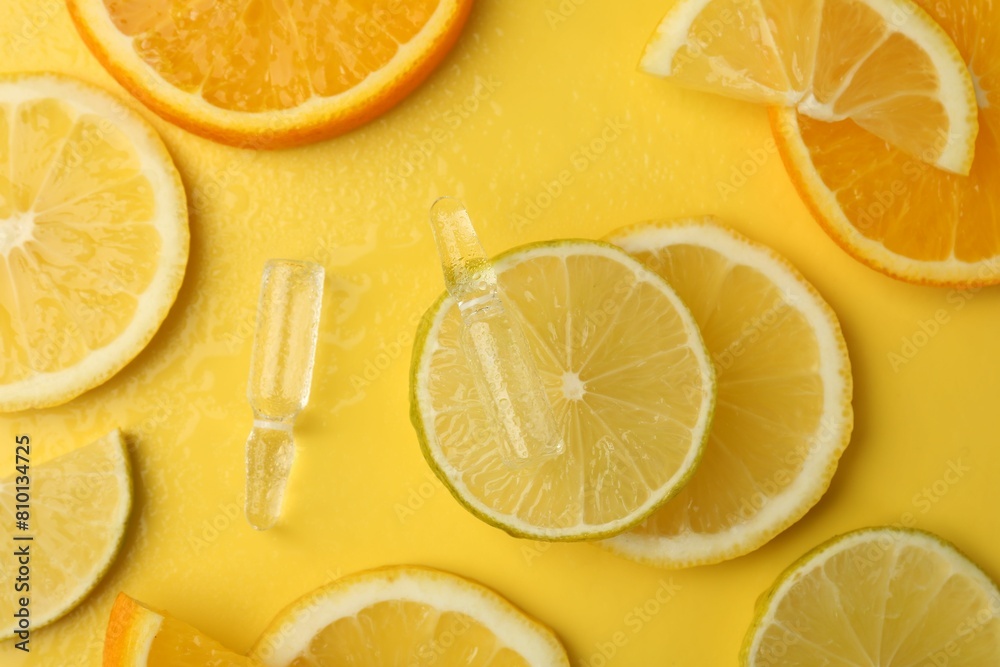 Skincare ampoules with vitamin C and citrus slices on yellow background, flat lay