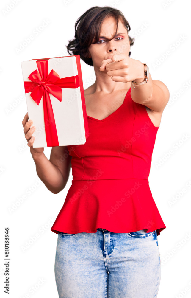 Beautiful young woman with short hair holding gift pointing with finger to the camera and to you, confident gesture looking serious Beautiful young woman with short hair holding gift pointing with finger to the camera and to you, confident gesture looking serious