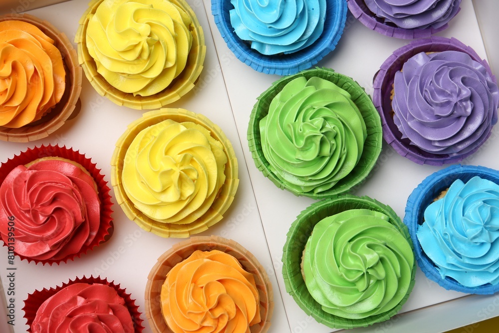 Many tasty cupcakes with colorful cream in box, top view