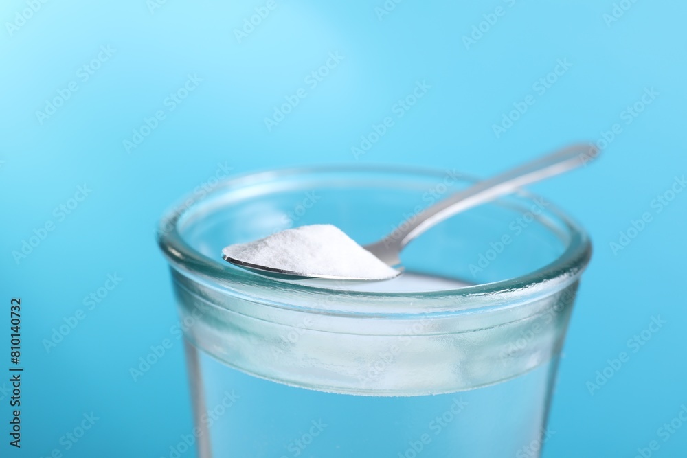 Glass of water and spoon with baking soda on light blue background, closeup