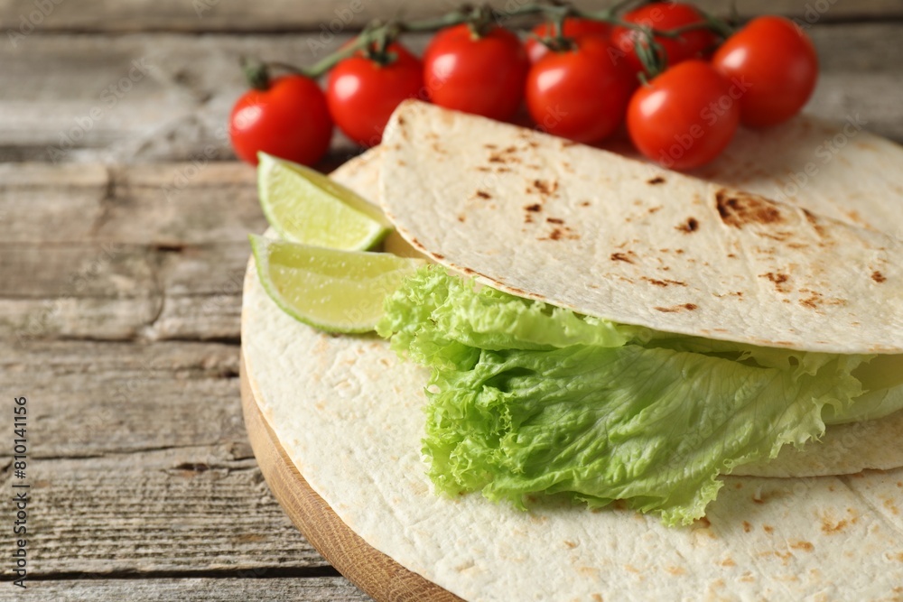 Tasty homemade tortillas, tomatoes, lime and lettuce on wooden table, closeup Tasty homemade tortillas, tomatoes, lime and lettuce on wooden table, closeup