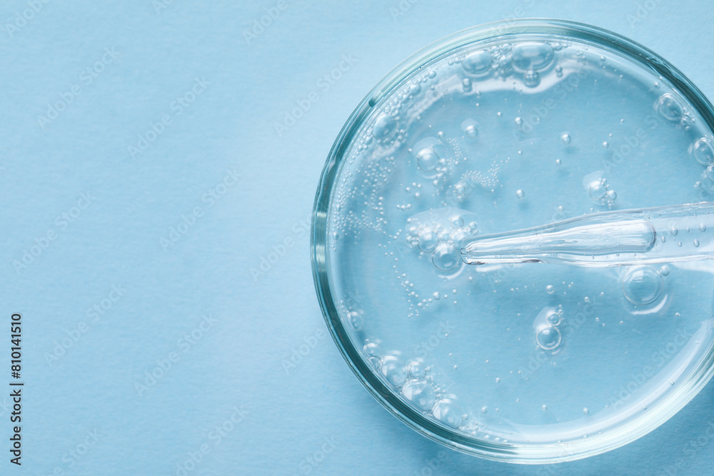 Glass pipette and petri dish with liquid on light blue background, top view. Space for text Glass pipette and petri dish with liquid on light blue background, top view. Space for text