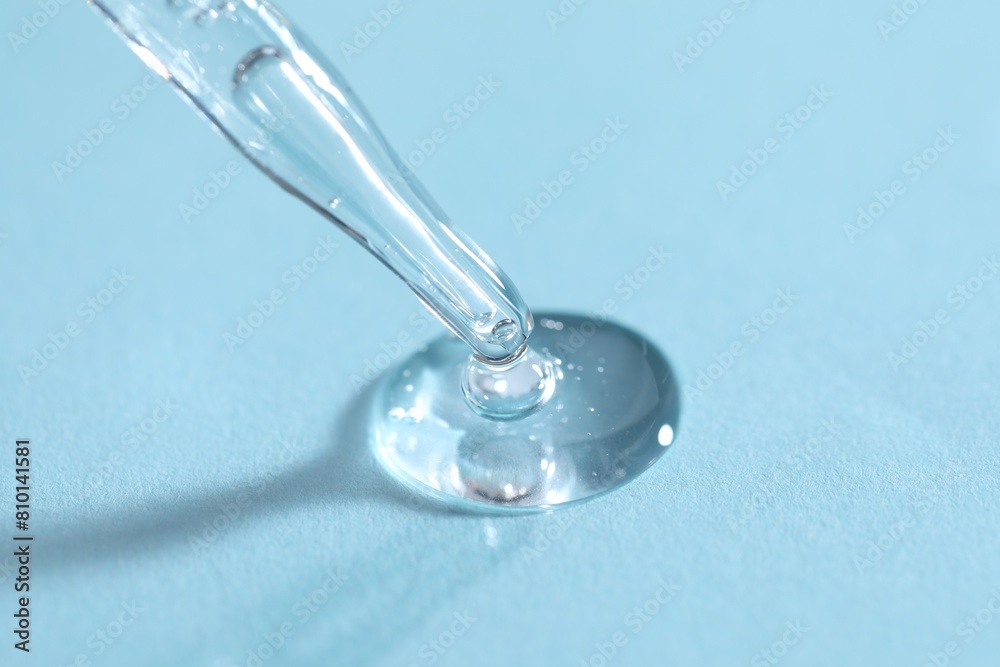 Glass pipette and transparent liquid on light blue background, closeup Glass pipette and transparent liquid on light blue background, closeup