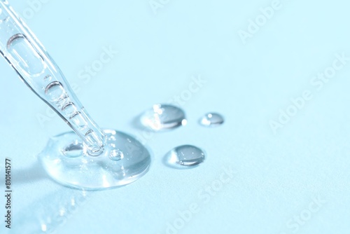 Glass pipette and transparent liquid on light blue background, closeup. Space for text © New Africa