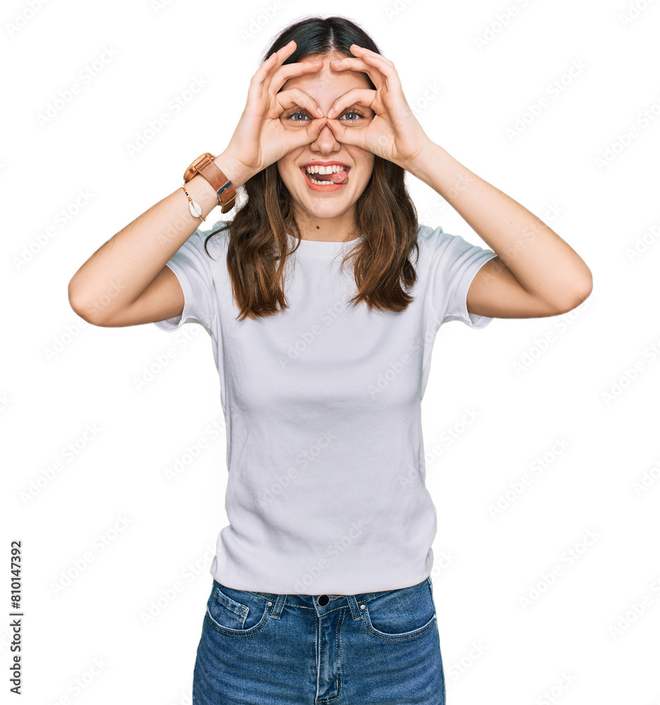 Young beautiful woman wearing casual white t shirt doing ok gesture like binoculars sticking tongue out, eyes looking through fingers. crazy expression. Young beautiful woman wearing casual white t shirt doing ok gesture like binoculars sticking tongue out, eyes looking through fingers. crazy expression.