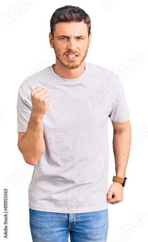 Handsome young man with bear wearing casual tshirt angry and mad raising fist frustrated and furious while shouting with anger. rage and aggressive concept.