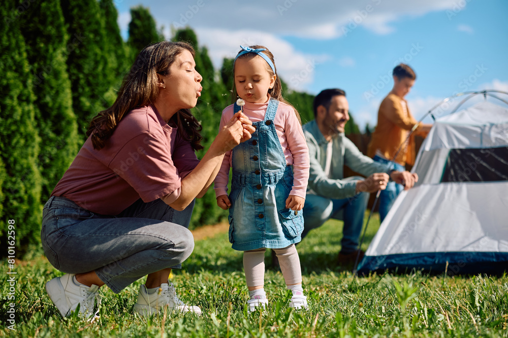Fototapeta premium Little girl and her mother blowing dandelion during family day in nature.