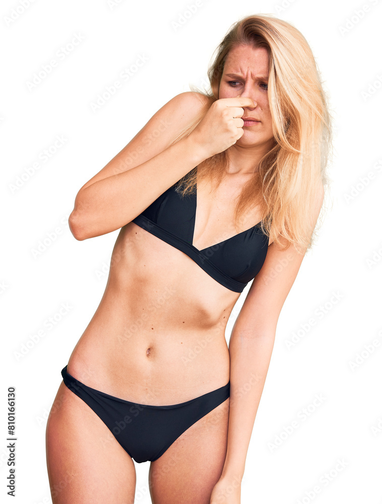 Young beautiful blonde woman wearing bikini smelling something stinky and disgusting, intolerable smell, holding breath with fingers on nose. bad smell Young beautiful blonde woman wearing bikini smelling something stinky and disgusting, intolerable smell, holding breath with fingers on nose. bad smell