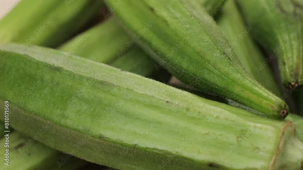 A staple food ingredient, okra, a natural food, is being cut in half on a wooden cutting board. This terrestrial plant is a common vegetable in cuisine. Close-up of A staple food ingredient, okra, a natural food, is being cut in half on a wooden cutting board. This terrestrial plant is a common vegetable in cuisine. Close-up of