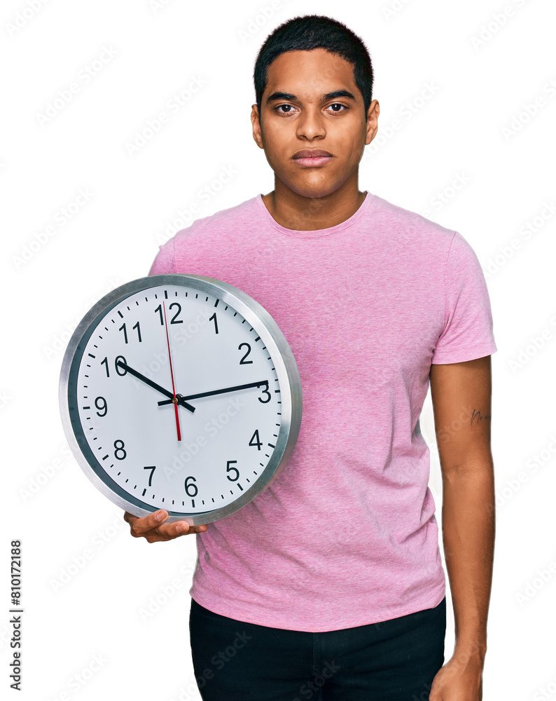 Young handsome hispanic man holding big clock thinking attitude and sober expression looking self confident Young handsome hispanic man holding big clock thinking attitude and sober expression looking self confident