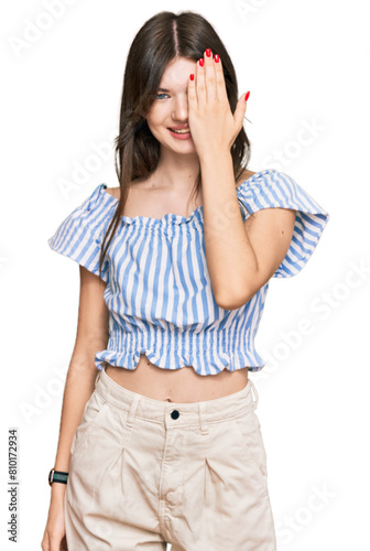 Young beautiful caucasian girl wearing casual clothes covering one eye with hand, confident smile on face and surprise emotion. © Krakenimages.com