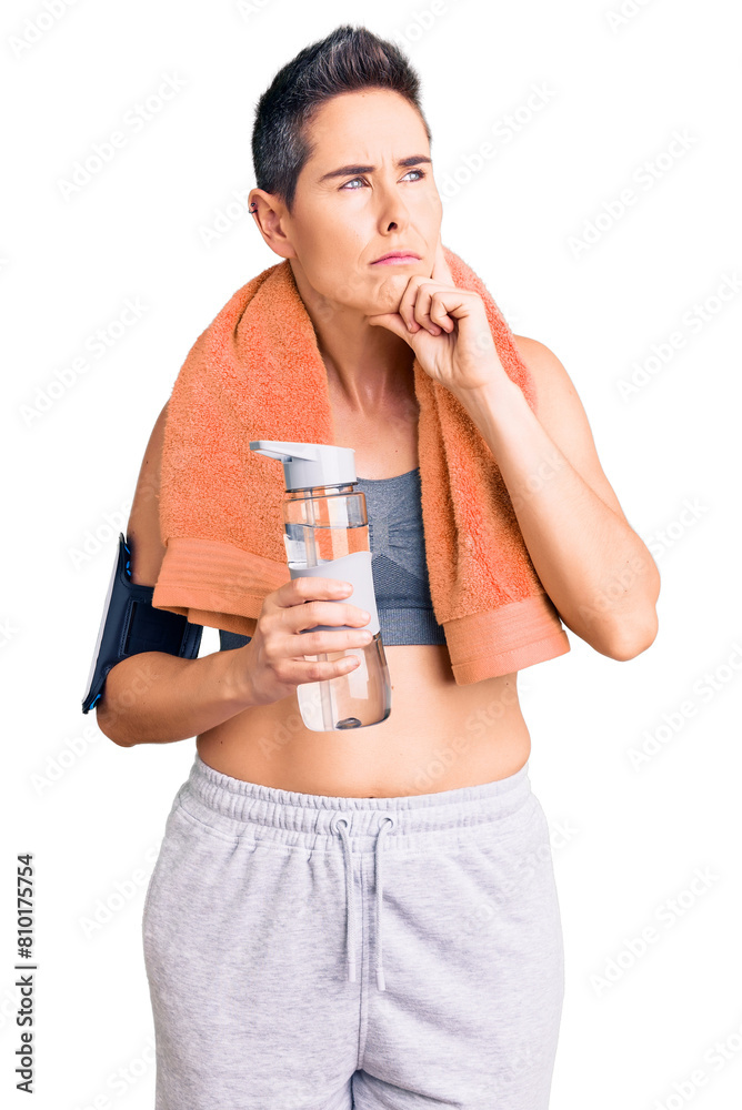 Young woman with short hair wearing sportswear and towel holding bottle of water serious face thinking about question with hand on chin, thoughtful about confusing idea Young woman with short hair wearing sportswear and towel holding bottle of water serious face thinking about question with hand on chin, thoughtful about confusing idea
