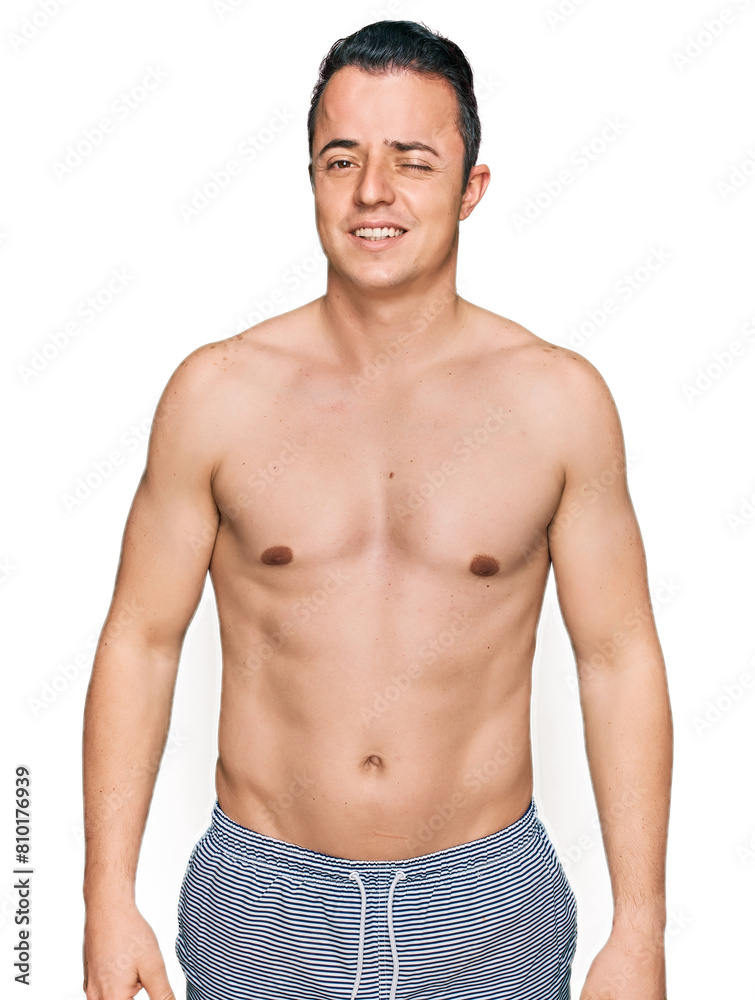 Handsome young man wearing swimwear shirtless winking looking at the camera with sexy expression, cheerful and happy face. Handsome young man wearing swimwear shirtless winking looking at the camera with sexy expression, cheerful and happy face.