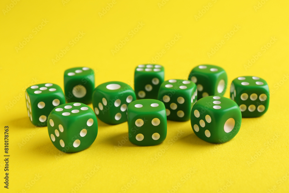 Many green game dices on yellow background, closeup Many green game dices on yellow background, closeup