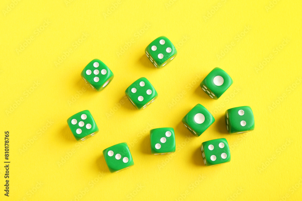 Many green game dices on yellow background, flat lay