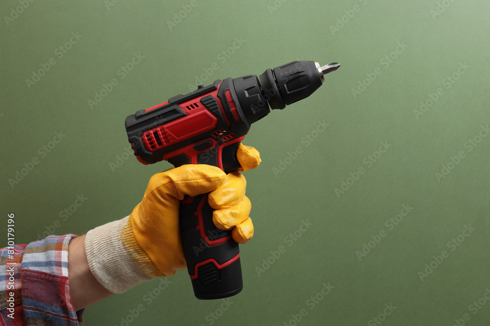Handyman holding electric screwdriver on pale green background, closeup