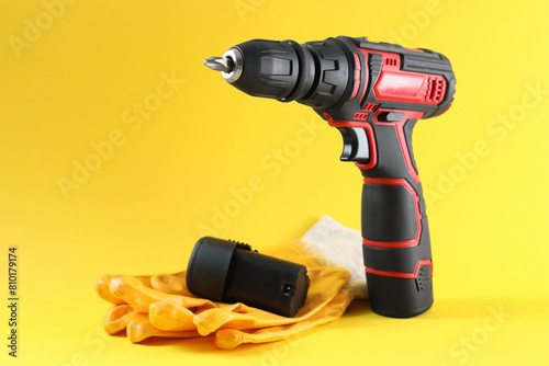Modern electric screwdriver, battery and gloves on yellow background