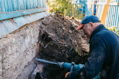 male worker drills the foundation with a hammer drill for sewerage in a country house. photo