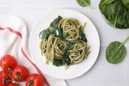 Tasty pasta with spinach  sauce and tomatoes on white tiled table  flat lay
