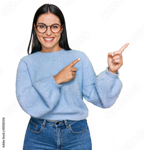 Young hispanic woman wearing casual clothes and glasses smiling and looking at the camera pointing with two hands and fingers to the side.