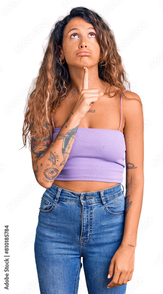 Young hispanic woman with tattoo wearing casual clothes thinking concentrated about doubt with finger on chin and looking up wondering Young hispanic woman with tattoo wearing casual clothes thinking concentrated about doubt with finger on chin and looking up wondering