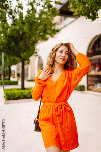 Beautiful young woman wearing nice orange dress walking on the street. Concept of lifestyle, fashion, travel. © maxbelchenko