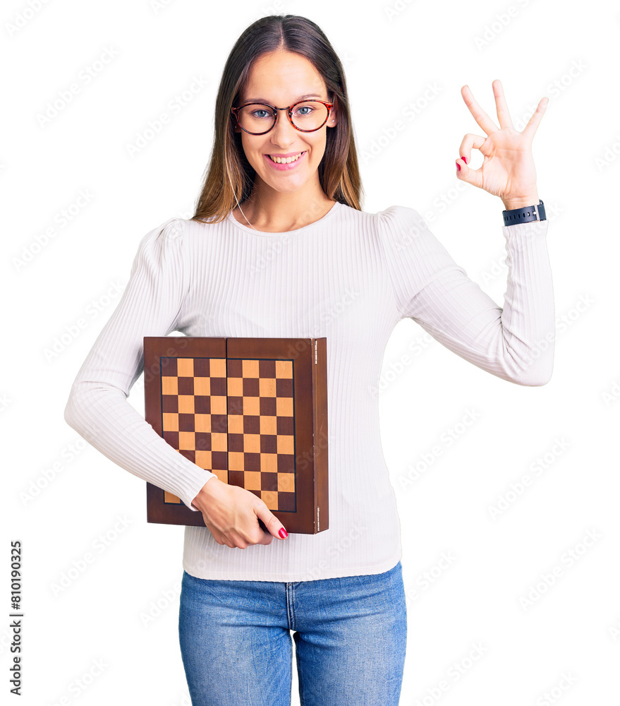 Beautiful brunette young woman holding chess doing ok sign with fingers, smiling friendly gesturing excellent symbol Beautiful brunette young woman holding chess doing ok sign with fingers, smiling friendly gesturing excellent symbol