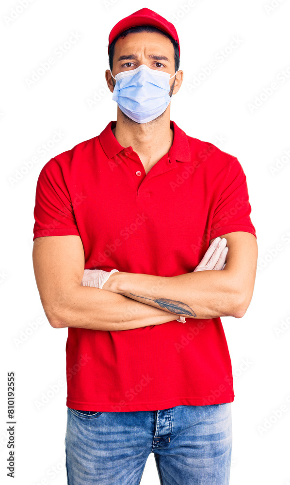 Young handsome hispanic man wearing delivery uniform and medical mask skeptic and nervous, disapproving expression on face with crossed arms. negative person. Young handsome hispanic man wearing delivery uniform and medical mask skeptic and nervous, disapproving expression on face with crossed arms. negative person.