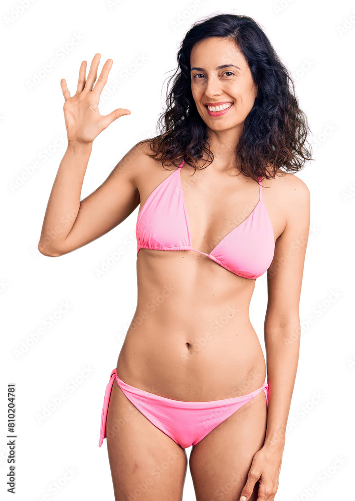 Young beautiful hispanic woman wearing bikini showing and pointing up with fingers number five while smiling confident and happy. Young beautiful hispanic woman wearing bikini showing and pointing up with fingers number five while smiling confident and happy.