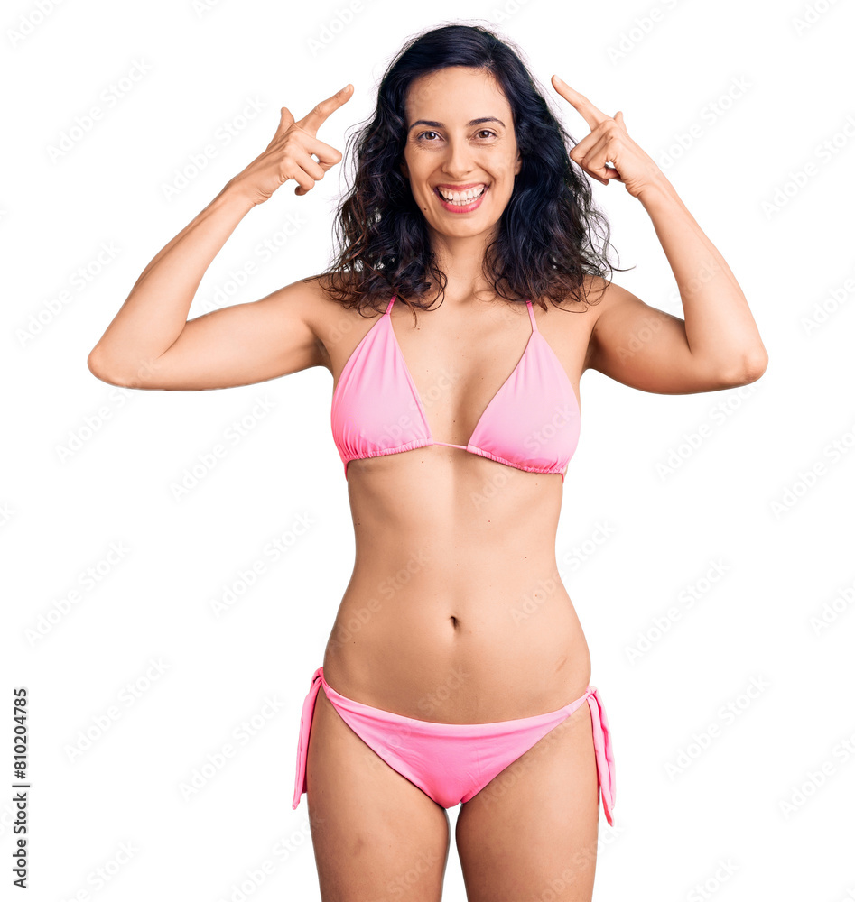 Young beautiful hispanic woman wearing bikini smiling pointing to head with both hands finger, great idea or thought, good memory Young beautiful hispanic woman wearing bikini smiling pointing to head with both hands finger, great idea or thought, good memory