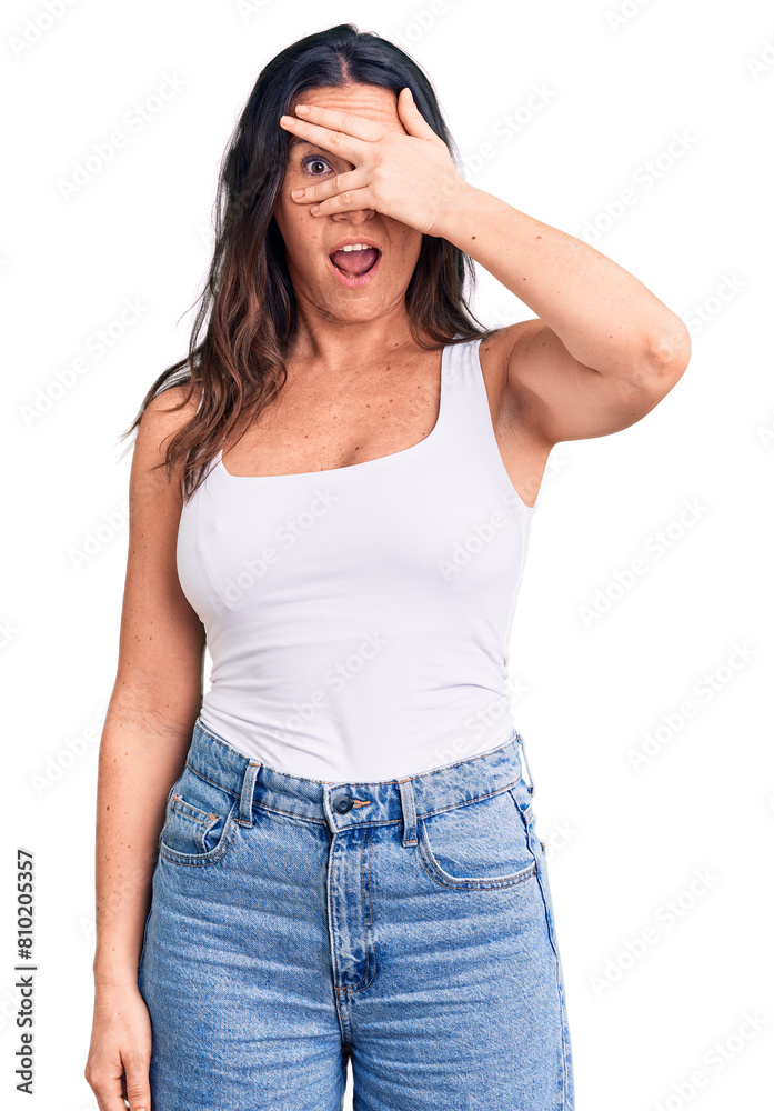 Young beautiful brunette woman wearing casual sleeveless t-shirt peeking in shock covering face and eyes with hand, looking through fingers with embarrassed expression. Young beautiful brunette woman wearing casual sleeveless t-shirt peeking in shock covering face and eyes with hand, looking through fingers with embarrassed expression.