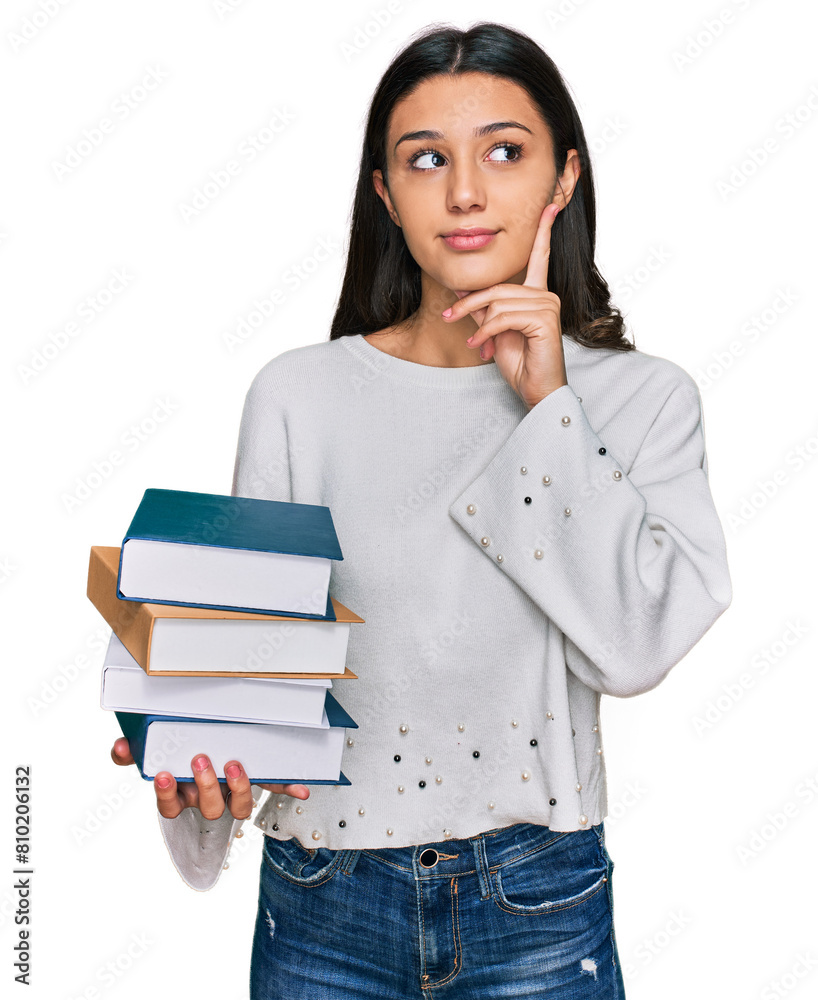 Young hispanic girl holding a pile of books serious face thinking about question with hand on chin, thoughtful about confusing idea Young hispanic girl holding a pile of books serious face thinking about question with hand on chin, thoughtful about confusing idea