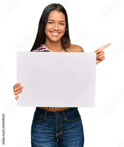 Beautiful hispanic woman holding blank empty banner smiling happy pointing with hand and finger to the side