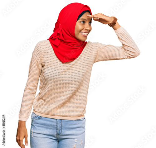 Young african american woman wearing traditional islamic hijab scarf very happy and smiling looking far away with hand over head. searching concept.