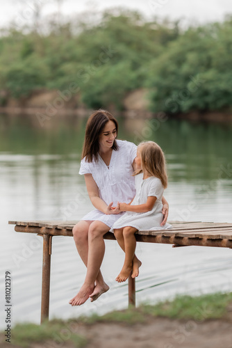 Mom and daughter sit on a wooden lake bridge in summer, Mother's Day