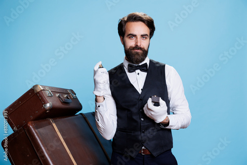 Stylish bellhop applying perfume, using strong bottle of cologne for rich luxurious scent and posing on camera. Professional doorman smelling like aromatic masculine spray, formal clothes. photo