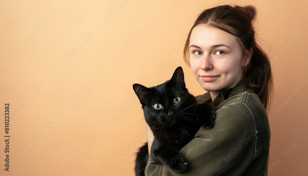 Young woman holding a black cat, friendly expression against an orange background Young woman holding a black cat, friendly expression against an orange background