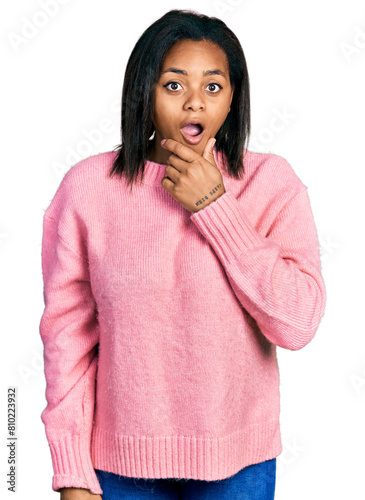 Beautiful hispanic woman wearing casual winter sweater looking fascinated with disbelief, surprise and amazed expression with hands on chin