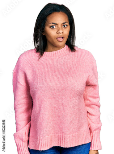 Beautiful hispanic woman wearing casual winter sweater in shock face, looking skeptical and sarcastic, surprised with open mouth