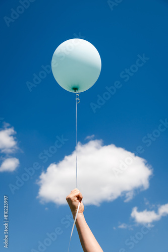 A child is holding a balloon on a string. Air balloon on the background of the sky. Rise to the sky. Light, weightless. Holiday concept. Happy Birthday- an inscription on a balloon. Great mood. Dream.