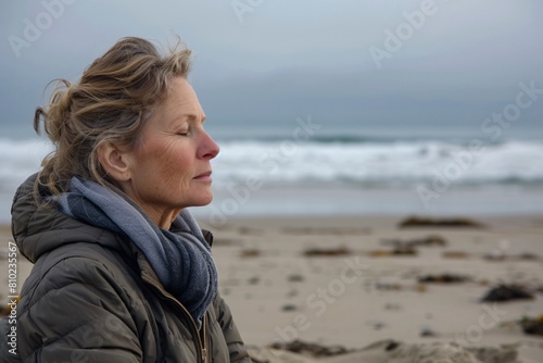A middle-aged woman peacefully meditating on a secluded beach, attuned to the sound of waves and the salty scent of the sea breeze photo