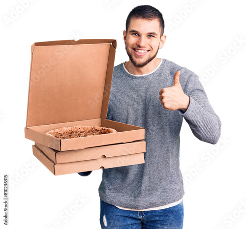 Young handsome man holding delivery italian pizza boxes smiling happy and positive, thumb up doing excellent and approval sign photo