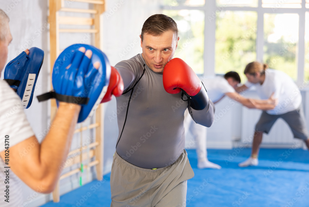 Man in boxing training practices punches with man in mitts in sport club
